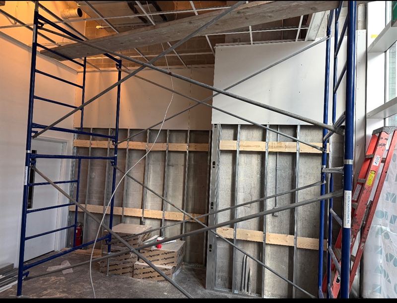 Two-storey drywall installation from scaffolding over furred masonry wall