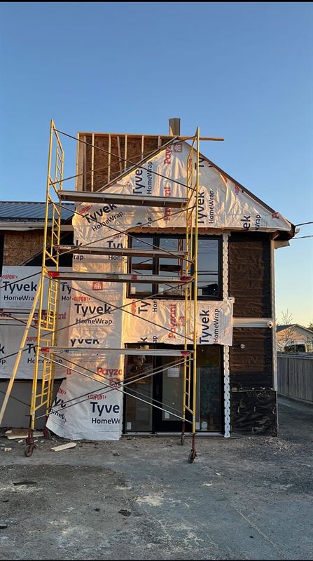 Residential addition wrapped in weather barrier with scaffolding at sunset