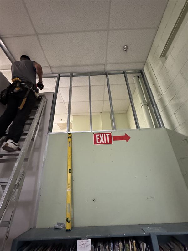 Worker on a ladder framing a partition above the ceiling line